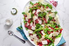 a white plate topped with salad next to a fork and spoon on top of a table