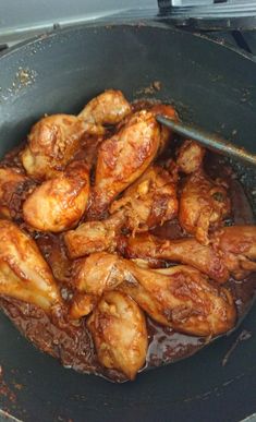 chicken is cooking in a skillet on the stove top with brown sauce over it