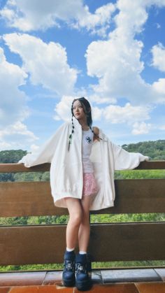 a young woman standing on top of a wooden bench next to a lush green field