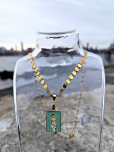 This vibrant Venus de Milo necklace features an exquisite enamel charm of the iconic Greek goddess. Suspended from a gorgeous golden disc chain, the rectangular charm captures the elegant curves of the statue set against a teal background. The necklace is made of gold-plated brass and has a lobster clasp closure. The Venus de Milo, also known as Aphrodite of Milos, is a renowned ancient Greek statue created between 130 and 100 BCE. Depicting the goddess of love and beauty, the statue is celebrated for its graceful lines and timeless beauty. It is currently displayed in the Louvre Museum in Paris. Our Venus de Milo necklace is a perfect tribute to this beloved artwork and is sure to capture the attention of any admirer of classical art. Venus Necklace, Museum In Paris, The Louvre Museum, Gold Disc Necklace, Necklace Art, Museums In Paris, Teal Background, Goddess Of Love, Louvre Museum