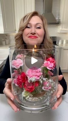 a woman holding up a vase with flowers in it and a lit candle on top