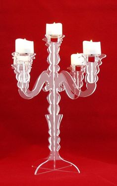 a clear candle holder with four candles on the top and one in the middle, against a red background