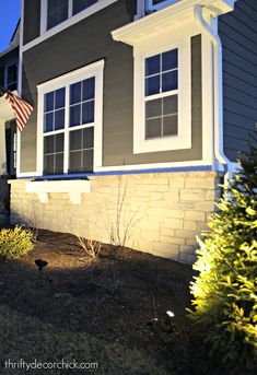 an american flag is in front of a gray house with white windows and shutters