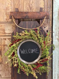 a welcome sign hanging from the side of a wooden door with a wreath on it