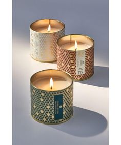 three lit candles sitting next to each other on a white surface with the lid open