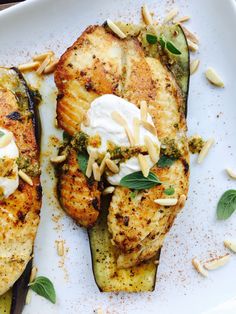 two grilled eggplant topped with yogurt and almonds on a white plate