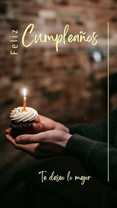 a person holding a cupcake with a candle in it and the words feliz cumpleanos