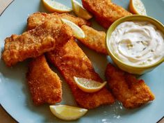 fish sticks with dipping sauce and lemon wedges on a blue plate, ready to be eaten