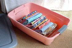 a pink plastic container filled with lots of cloths on top of a carpeted floor