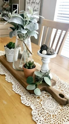 a wooden table topped with potted plants on top of a white doily covered table