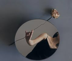 a woman's reflection in a round mirror with a flower on the wall next to it