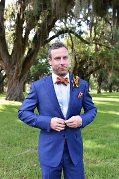 a man wearing a blue suit and bow tie standing in the grass with his hands on his hips