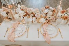 the table is set with white and gold plates, silverware, and pink flowers