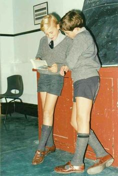 two young boys in school uniforms are sitting on a desk and looking at a book