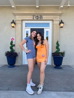 two women standing in front of a building with their arms around each other and smiling at the camera