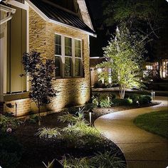 an outdoor walkway lit up at night in front of a house with landscaping and trees