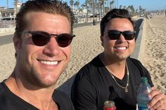 two men are sitting on the beach and one is holding a bottle of water in his hand