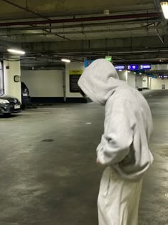 a person in a hoodie is standing in an empty parking garage with his back turned to the camera