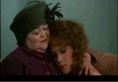 two women embracing each other on a couch in front of a green wall and one woman with red hair wearing a black hat