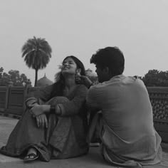 a man and woman sitting on the ground next to each other looking up into the sky