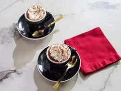 two cups of hot chocolate with whipped cream and gold spoons on a marble table