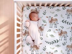 a baby is sleeping in a crib with farm animals on the wall behind it