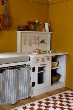 a toy kitchen with an oven, sink and stove top in the corner next to a rug