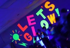 people are dancing in a dark room with neon lights on the walls and below them is a sign that says let's glow