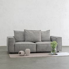 a gray couch sitting on top of a rug next to a vase and potted plant