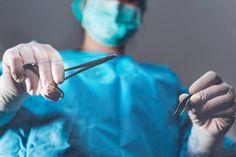 a person in scrubs is holding scissors and looking at the camera while wearing surgical gear