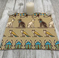 a candle sits on top of a napkin with egyptian cats and scarves printed on it