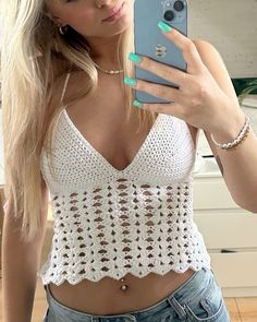 a woman taking a selfie with her cell phone in front of her face and wearing a white crocheted crop top