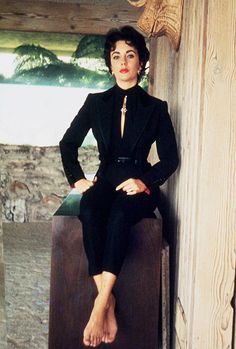 a woman sitting on top of a wooden bench in front of a wall and window