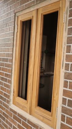 two windows on the side of a brick building with wood trim and glass panes