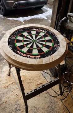 a wooden table with a dart on it in the middle of a garage floor next to a car