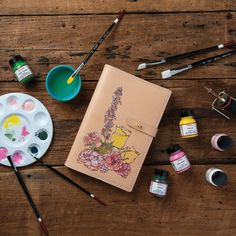 an artist's supplies on a wooden table including paint, watercolors and brushes