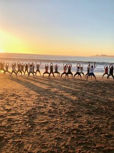 a group of people standing on top of a sandy beach next to the ocean with their arms in the air