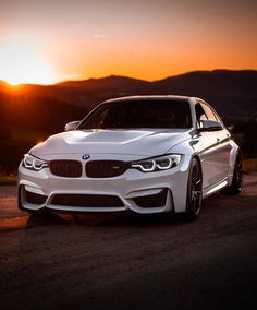 a white car parked on the side of a road at sunset with mountains in the background