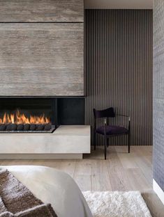 a modern bedroom with a fireplace in the middle and a chair next to it,