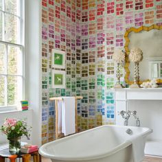 a bath tub sitting under a window next to a white wall covered in colorful tiles