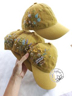 two hats with embroidered flowers on them being held up by a person's hand