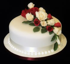 a white cake with red and white flowers on it's side, sitting on a table