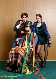 three people sitting on top of a wheel chair wearing party hats and streamers in front of them