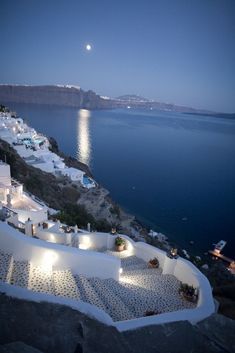 the moon shines brightly in the night sky over an island with white buildings and steps leading up to it