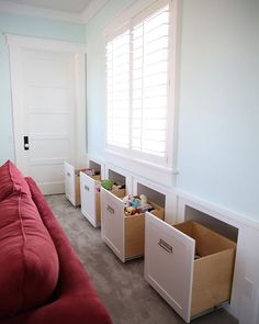 a red couch sitting in front of a window next to two bins filled with toys