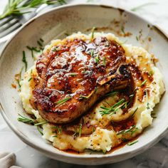 meat and mashed potatoes in a white bowl on a marble countertop with silverware