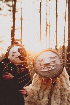 two people standing in the woods with their faces painted on them and some lights behind them