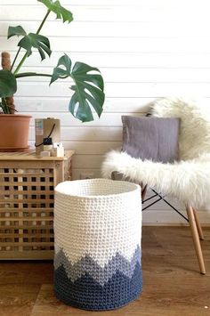 a white and blue crochet basket next to a plant in a room with wood flooring