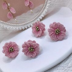 three pink crocheted flowers sitting on top of a white plate next to pearls