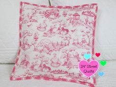 a pink and white pillow on top of a bed with hearts in the corner next to it